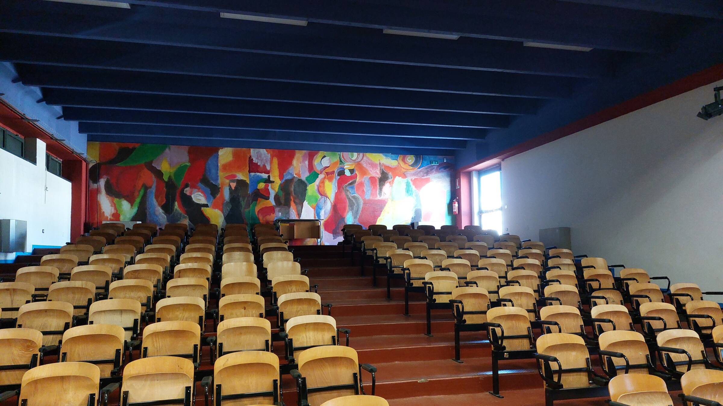 : Auditorium della scuola Don Tonino Bello a Rutigliano, con sedute disposte su gradoni e nervature della copertura a vista.